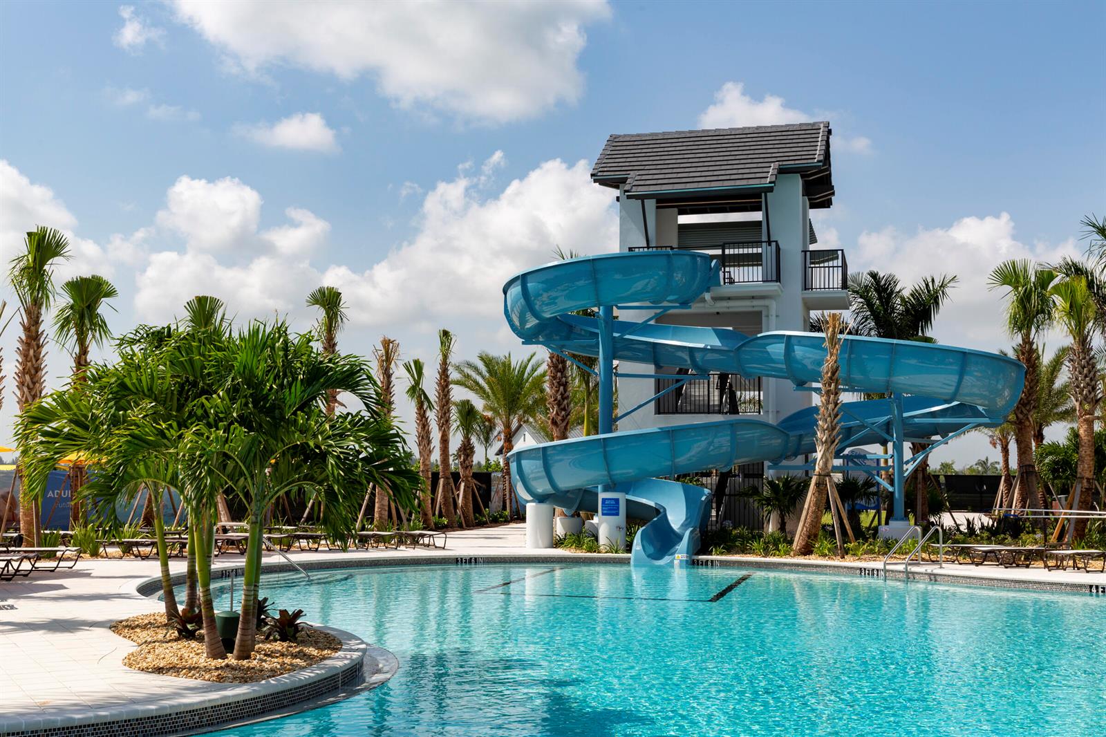 A blue water slide spirals down from a tower into a swimming pool with palm trees — 14141 Spruce Pine Drive, Westlake FL 33470, WESTLAKE, FL