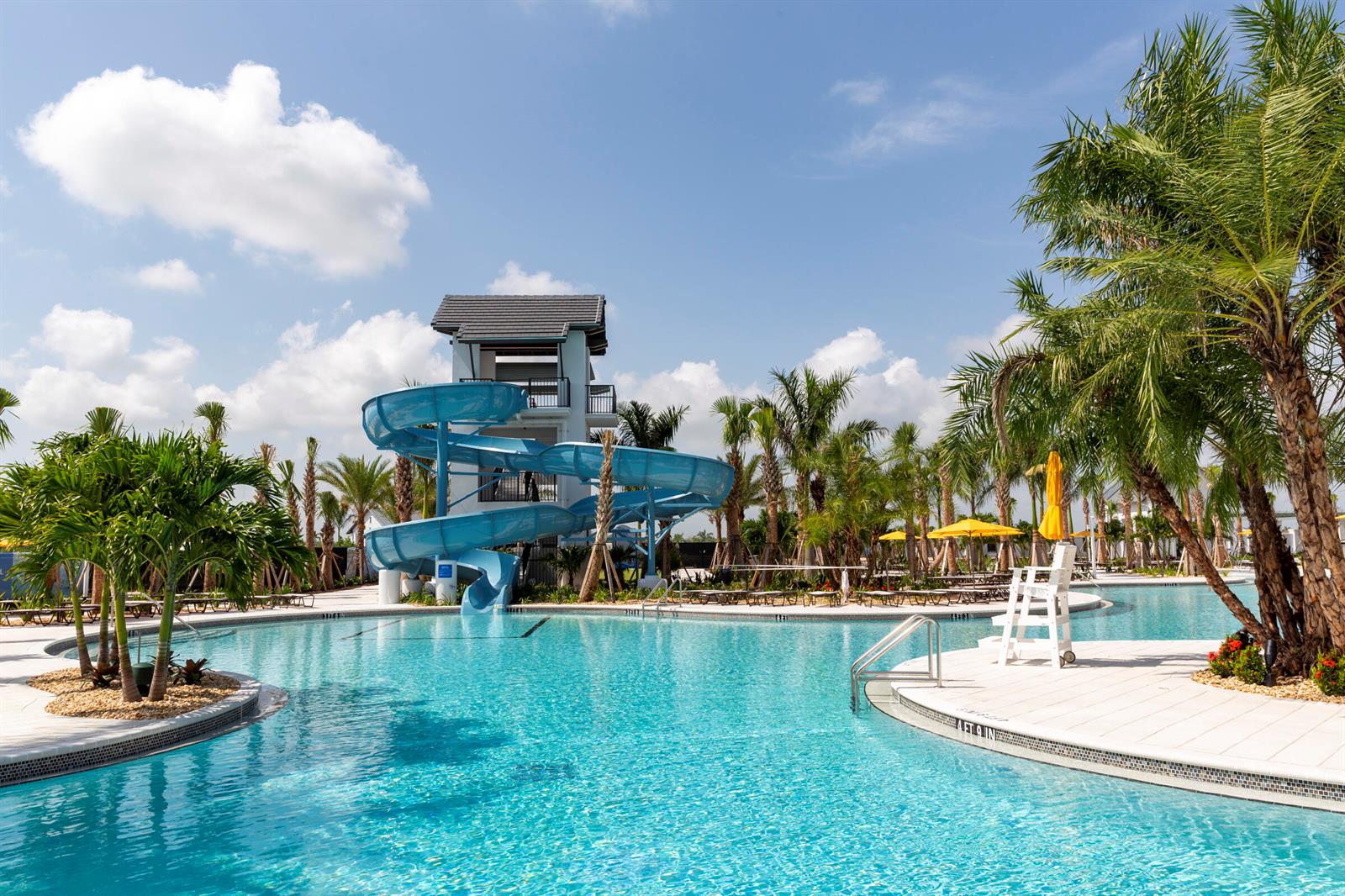 A swimming pool with a blue water slide and palm trees under a sunny sky — 14141 Spruce Pine Drive, Westlake FL 33470, WESTLAKE, FL