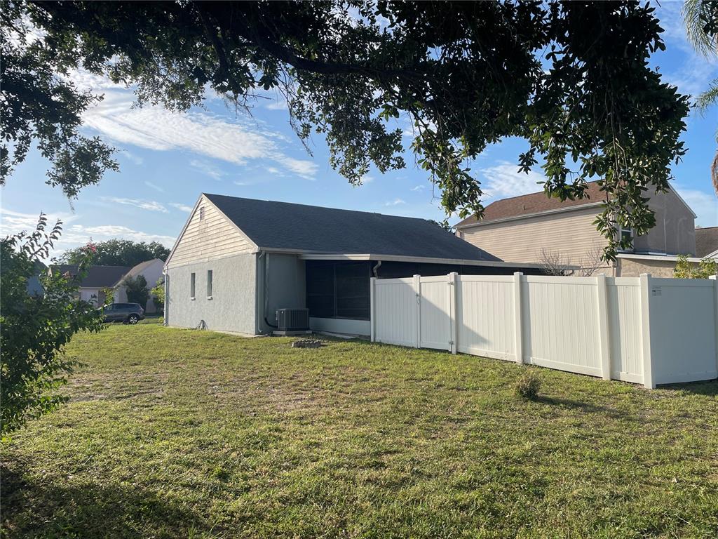 The exterior of a house features a gray stucco wall, a screened patio, and a fence — 11001 SUNSWEPT PLACE, TAMPA, FL