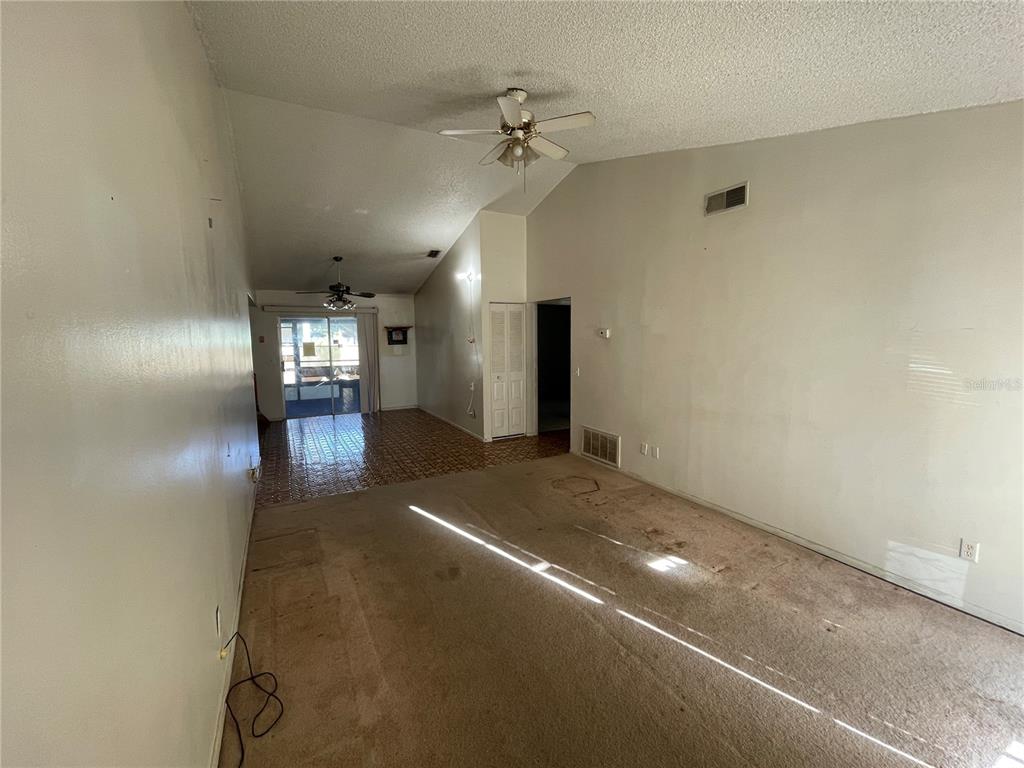 An empty living room features beige carpeting, a vaulted ceiling, and a tiled dining area — 11001 SUNSWEPT PLACE, TAMPA, FL