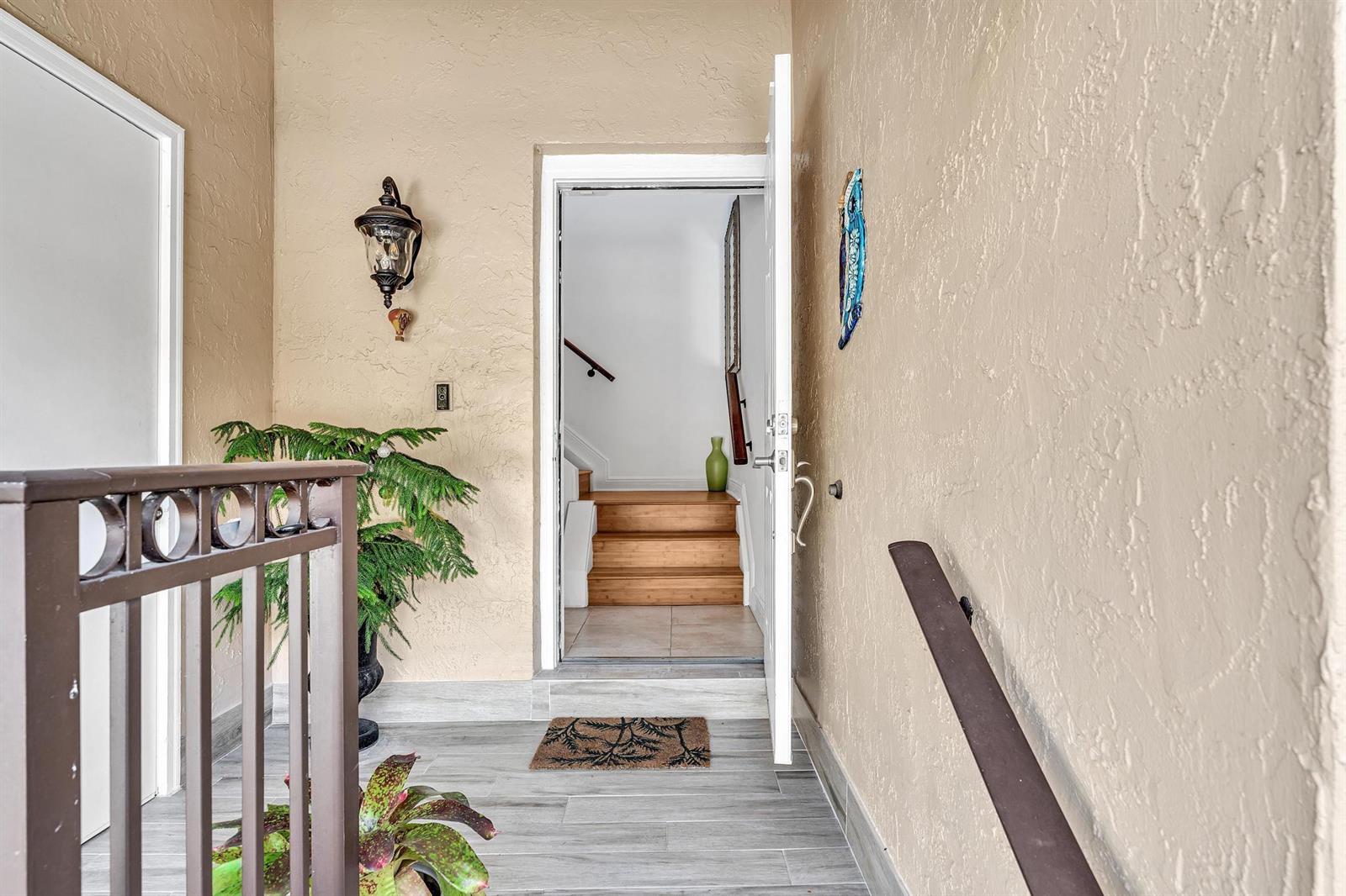 An entryway with light-colored walls, wood-look tile flooring, a staircase, and a metal railing — 6666 Montego Bay Boulevard # B, Boca Raton FL 33433, BOCA RATON, FL