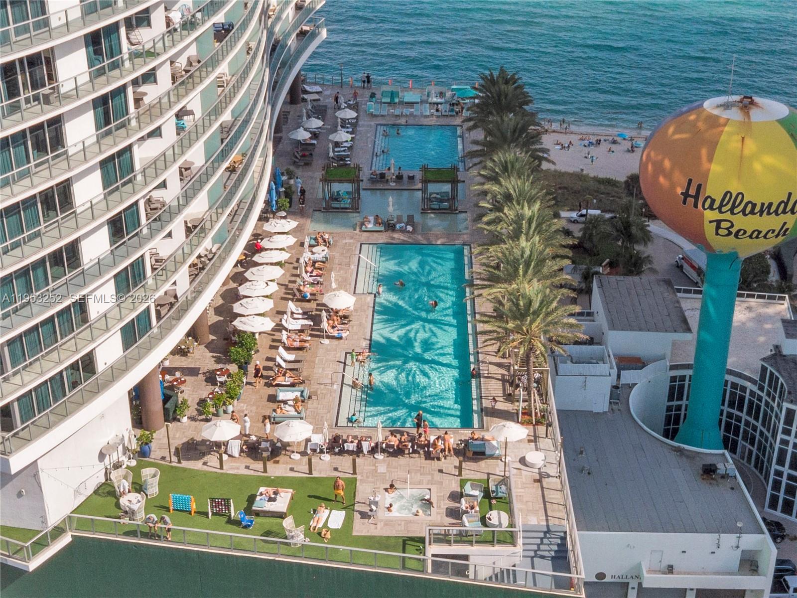 An aerial view shows a large resort pool deck with lounge chairs and palm trees — 4111 S Ocean Dr # 1507, Hollywood FL 33019, HOLLYWOOD, FL