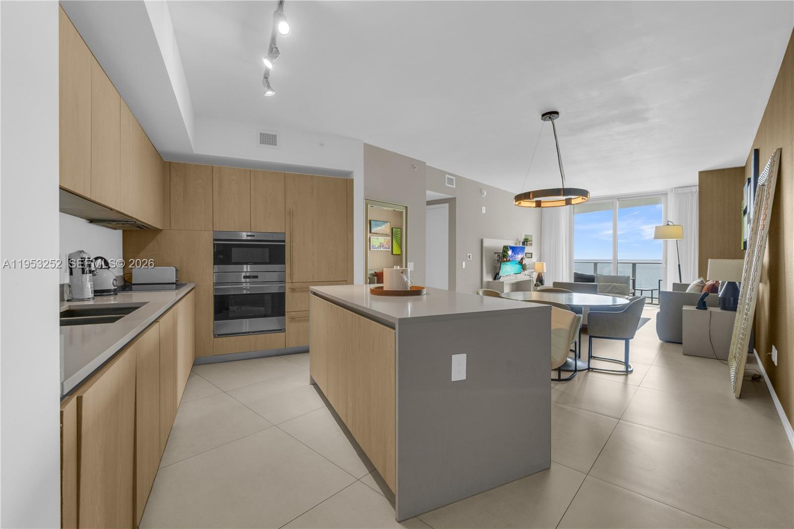 A modern kitchen with light wood cabinetry and a gray island opens to a living area — 4111 S Ocean Dr # 1507, Hollywood FL 33019, HOLLYWOOD, FL