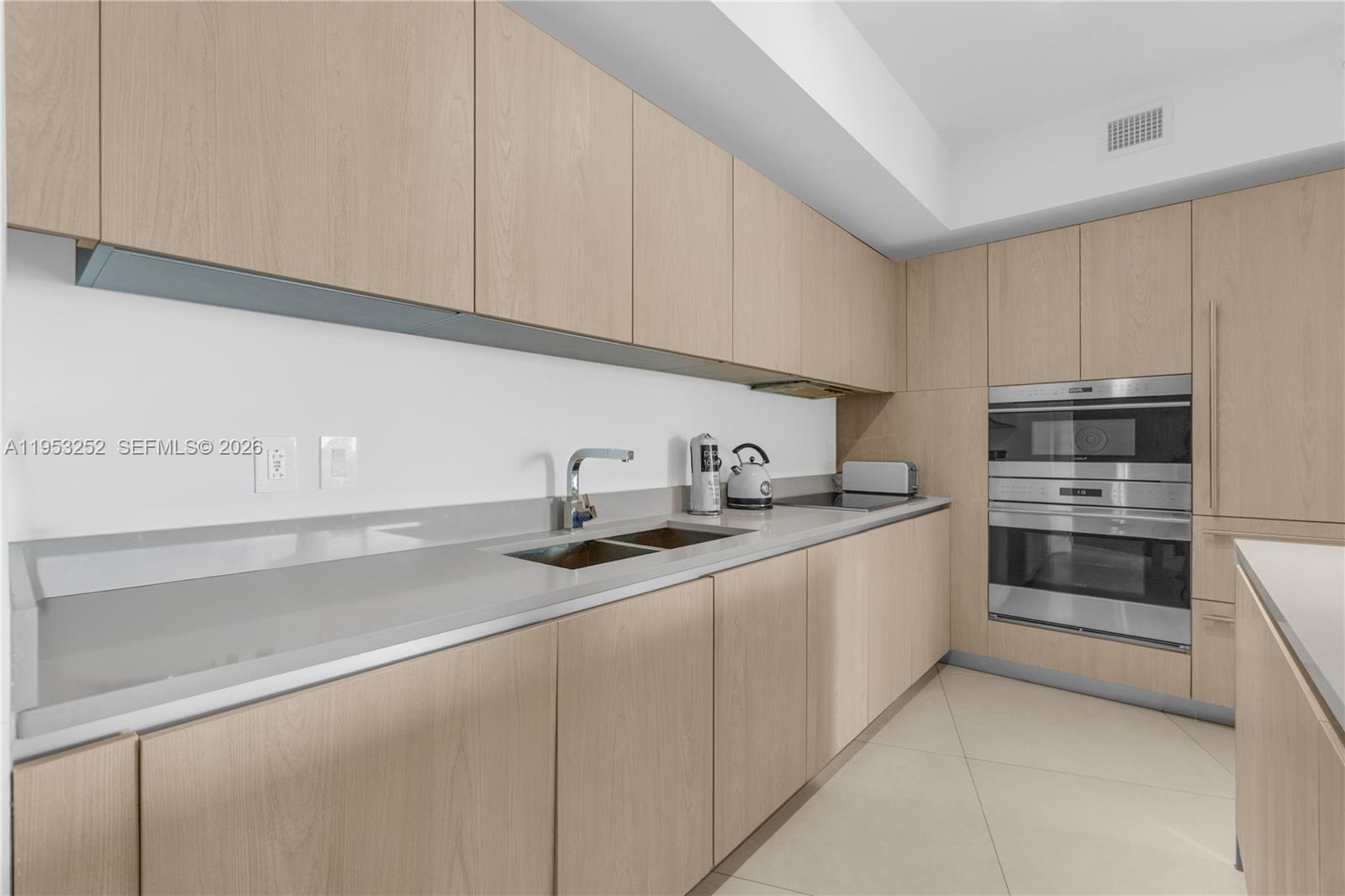 A modern kitchen features light wood cabinetry, stainless steel appliances, and gray stone countertops — 4111 S Ocean Dr # 1507, Hollywood FL 33019, HOLLYWOOD, FL