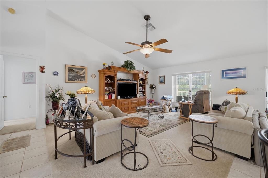 A living room features a vaulted ceiling, a ceiling fan, beige sofas, and a wooden entertainment center — 2384 LEMA DRIVE, SPRING HILL, FL