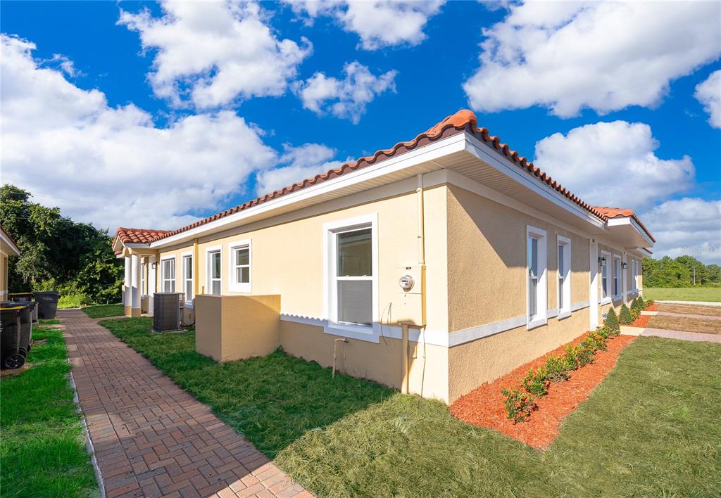 The exterior of a tan stucco building features a red tile roof and brick walkway — 1657 CUMIN DRIVE, KISSIMMEE, FL