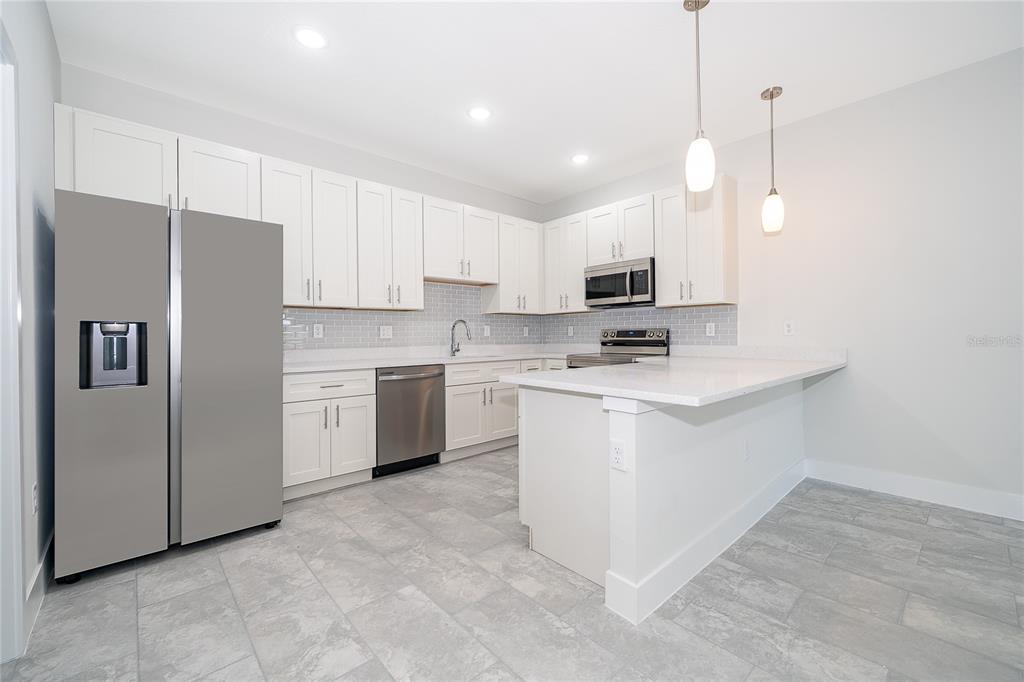 A modern kitchen features white cabinetry, stainless steel appliances, a breakfast bar, and gray flooring — 1657 CUMIN DRIVE, KISSIMMEE, FL