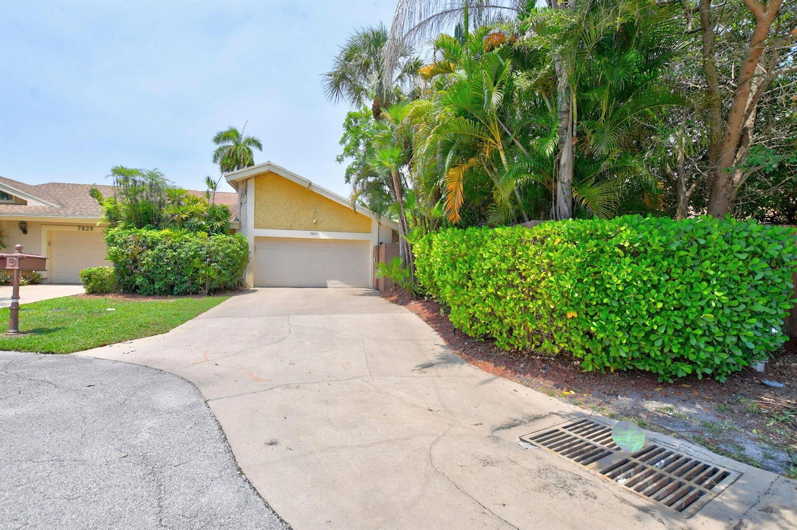A yellow house with a garage and driveway sits next to a large green hedge — 7813 Kenway Place W, Boca Raton FL 33433, BOCA RATON, FL