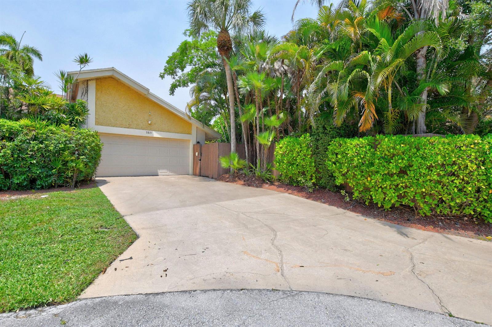 A concrete driveway leads to a one-car garage attached to a yellow house with landscaping — 7813 Kenway Place W, Boca Raton FL 33433, BOCA RATON, FL