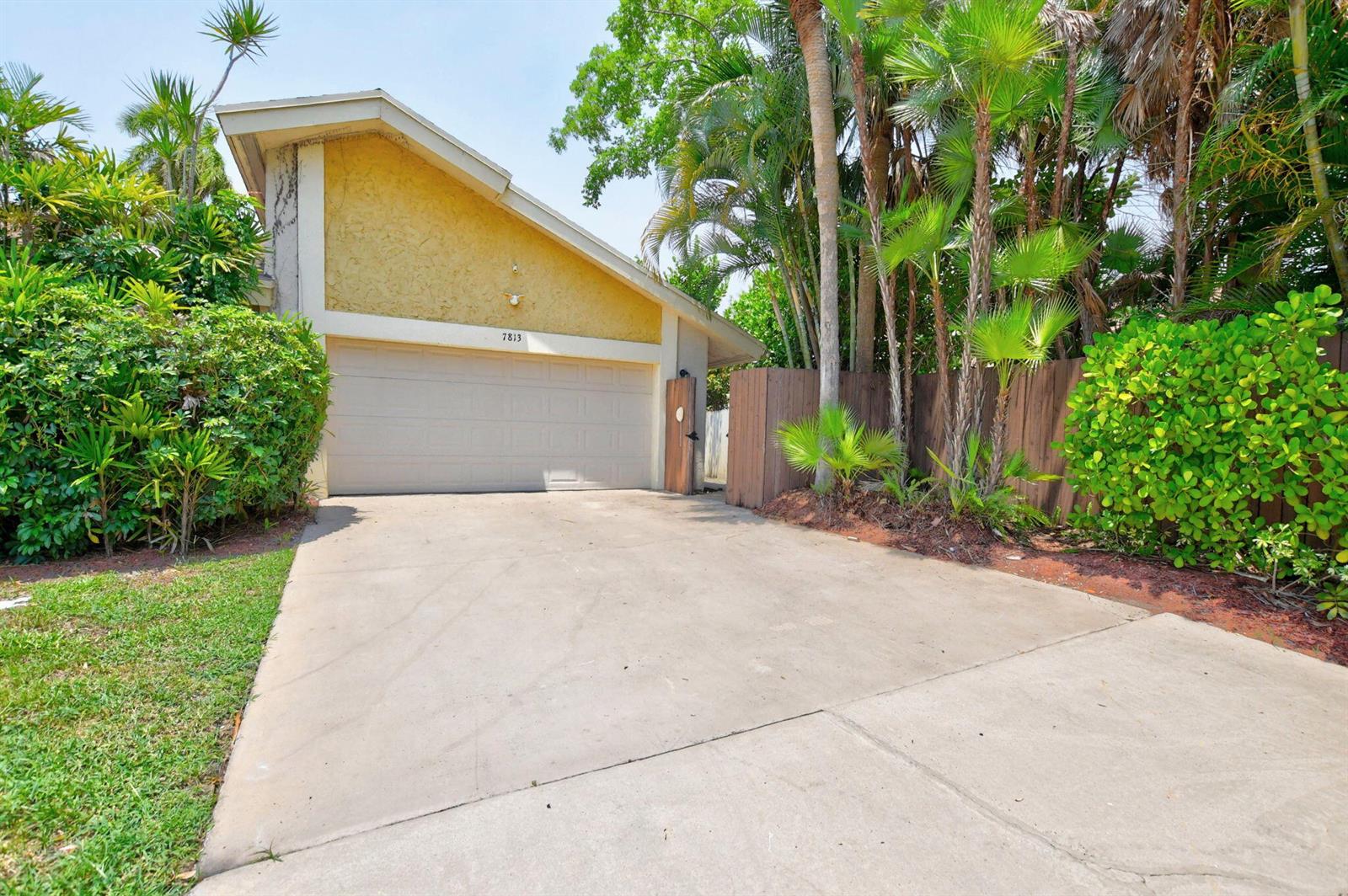 A concrete driveway leads to a single-story house with a yellow garage exterior — 7813 Kenway Place W, Boca Raton FL 33433, BOCA RATON, FL