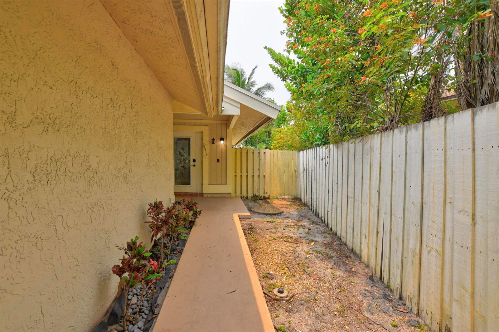 A concrete walkway leads to a front door alongside a wooden fence and landscaping — 7813 Kenway Place W, Boca Raton FL 33433, BOCA RATON, FL