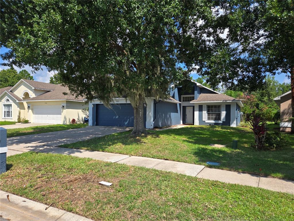 A blue single-story house with a two-car garage and a large tree in the yard — 19551 GLEN ELM WAY, ORLANDO, FL