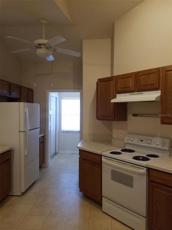 A kitchen features white appliances, wood cabinets, light countertops, and a ceiling fan — 19551 GLEN ELM WAY, ORLANDO, FL