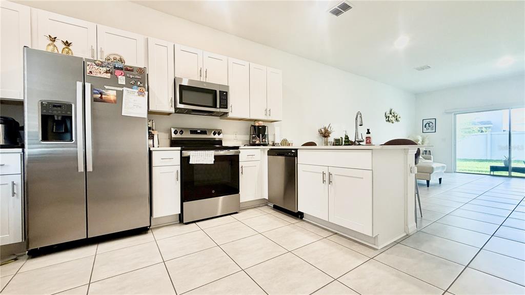 A modern kitchen features white cabinetry, stainless steel appliances, and a central island with seating — 3244 SKYLINE LOOP, KISSIMMEE, FL