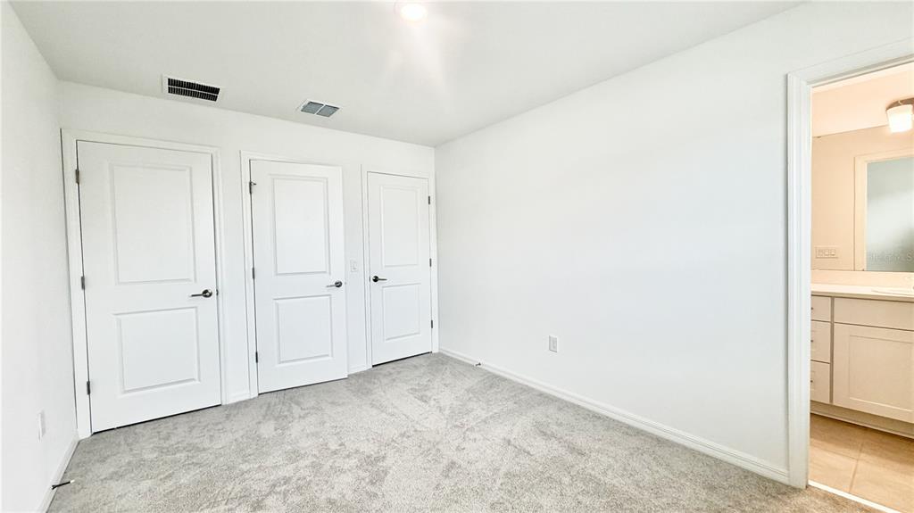 A bedroom with gray carpet, three white doors, and an adjacent bathroom doorway — 3244 SKYLINE LOOP, KISSIMMEE, FL