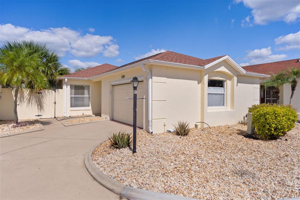 A single-story house with a beige stucco exterior, a garage, and a gravel front yard — 1330 LA JOLLA CIRCLE, THE VILLAGES, FL