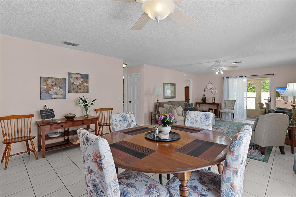 A dining area with a round wooden table and floral chairs opens into a living room — 1330 LA JOLLA CIRCLE, THE VILLAGES, FL