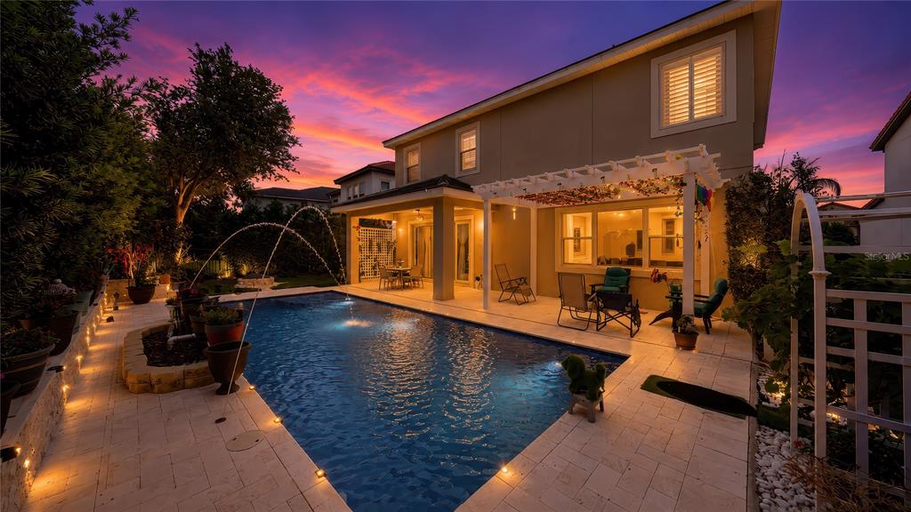 A backyard swimming pool with fountains and a pergola sits beside a two-story house — 15554 PANTHER LAKE DRIVE, WINTER GARDEN, FL