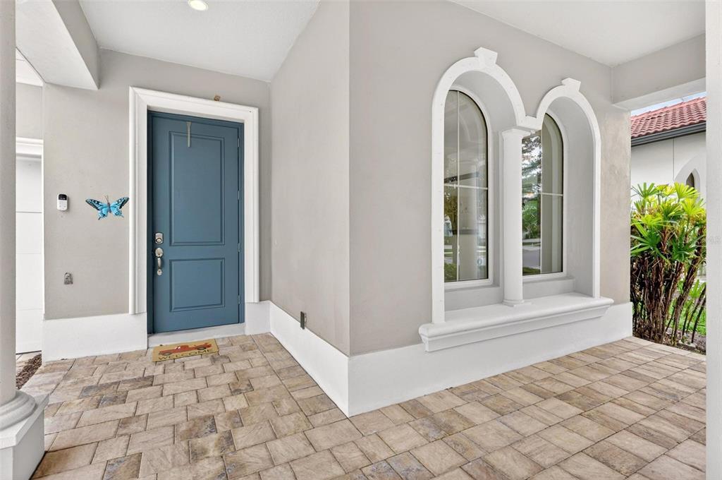 A covered entryway features a blue front door, arched windows, and stone paver flooring — 15554 PANTHER LAKE DRIVE, WINTER GARDEN, FL