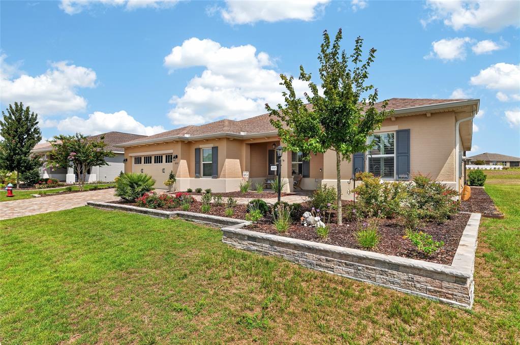 A tan single-story house with a stone-walled garden bed and a paved driveway — 9707 SW 103RD TERRACE, OCALA, FL
