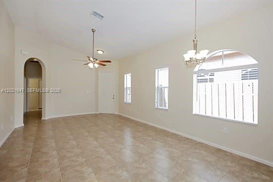A bright, empty living room features beige tile flooring, a ceiling fan, and arched windows — HOMESTEAD, FL