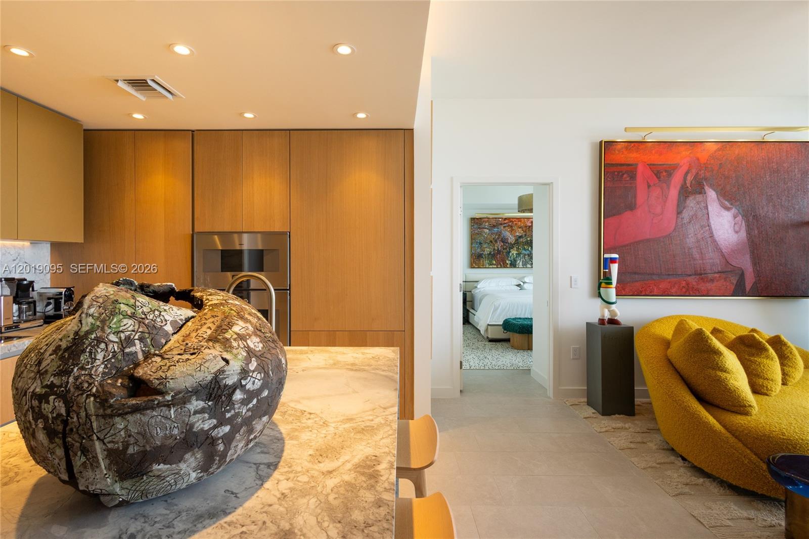 A modern kitchen with wood cabinetry and a marble island opens into a living area — 501 West Ave # 3404, Miami Beach FL 33139, MIAMI BEACH, FL