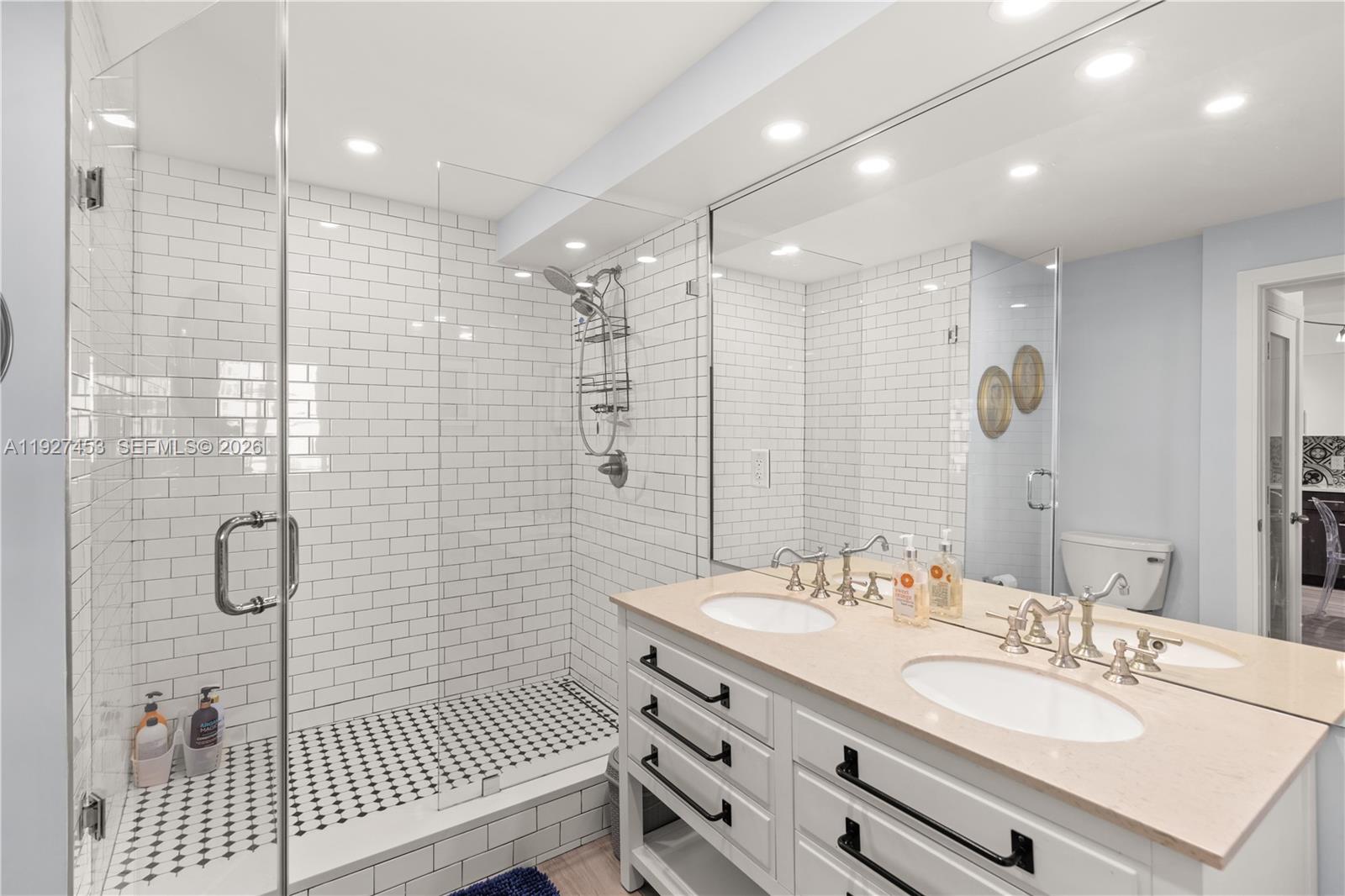A bathroom features a double vanity, a glass-enclosed shower with subway tiles, and a mirror — 100 Lincoln Rd # 643, Miami Beach FL 33139, MIAMI BEACH, FL