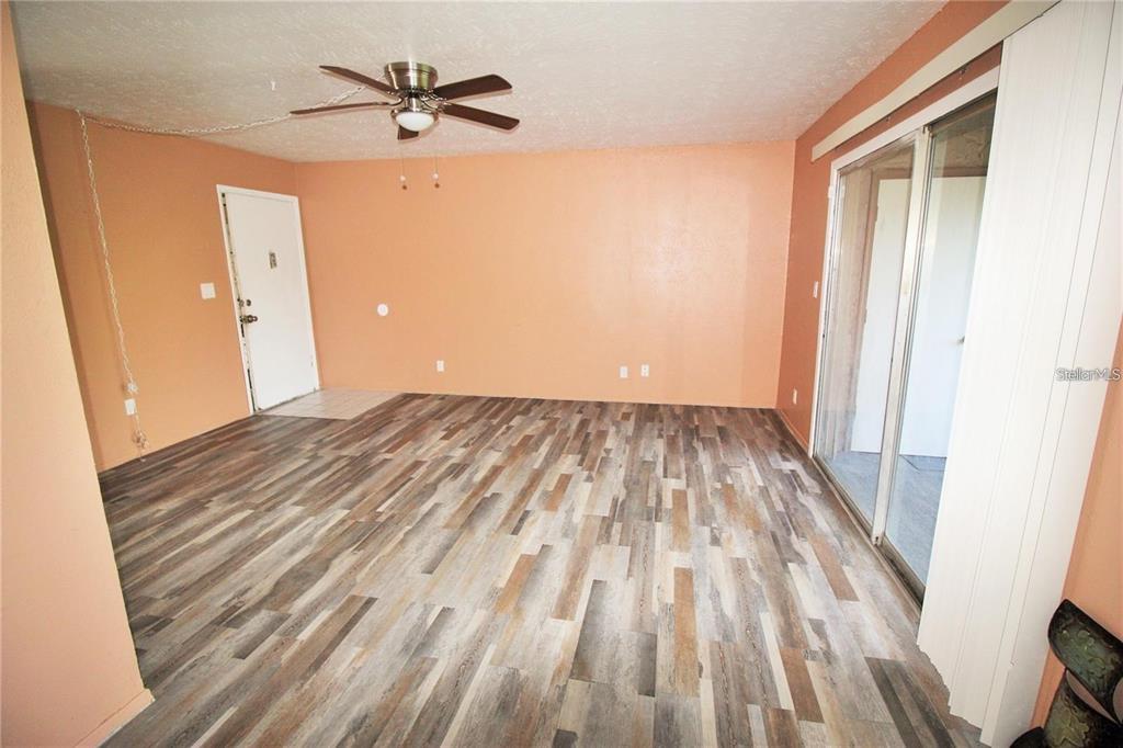 An empty room features peach-colored walls, wood-look flooring, a ceiling fan, and sliding glass doors — 2117 LYME BAY DRIVE UNIT 604, ORLANDO, FL
