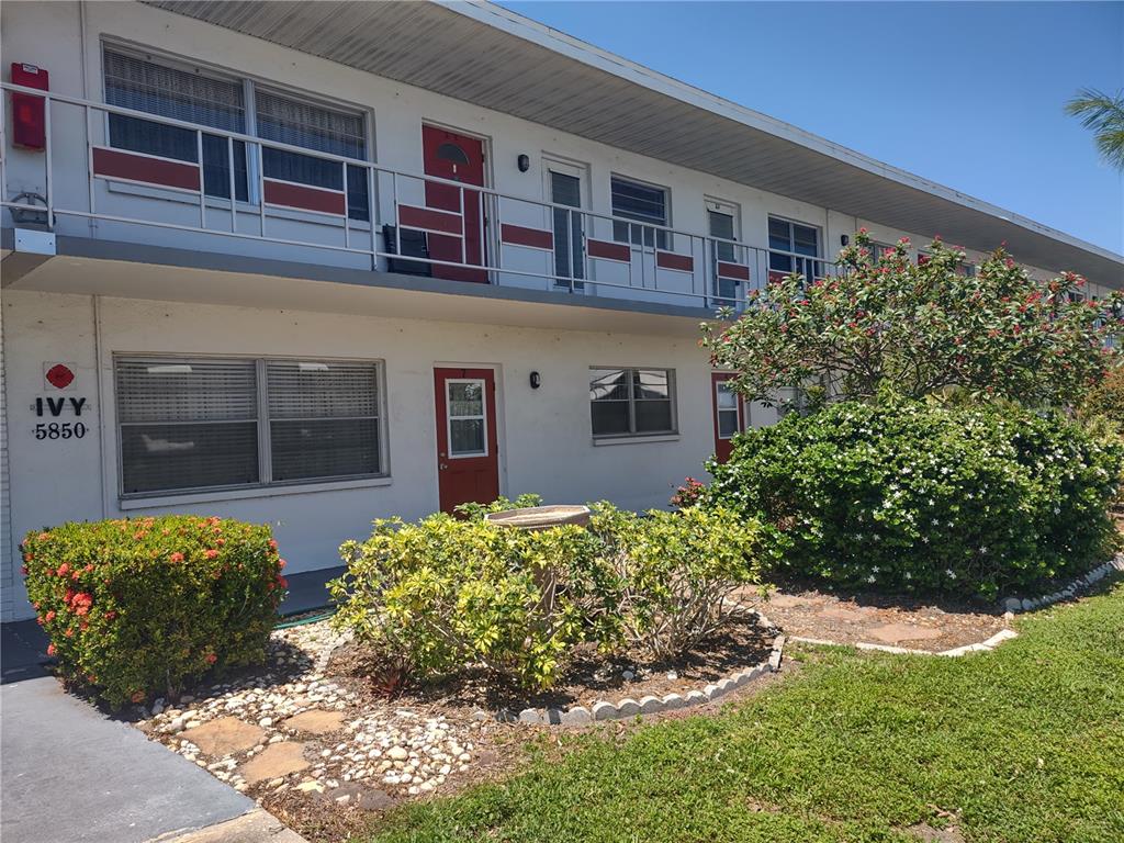 A two-story apartment building with red doors, white exterior walls, and landscaped front gardens — 5850 18TH STREET N UNIT 7, ST PETERSBURG, FL