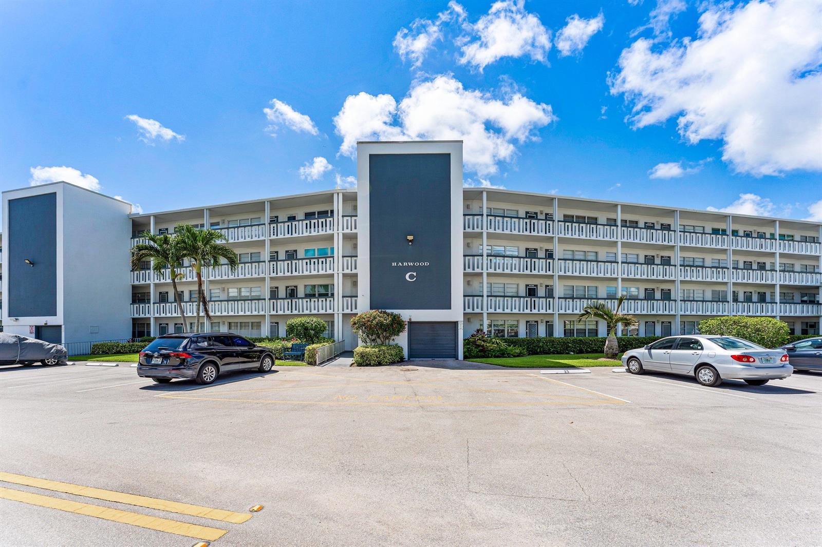 A multi-story apartment building exterior features a central dark blue facade labeled Harwood C — 1017 Harwood C, Deerfield Beach FL 33442, DEERFIELD BEACH, FL
