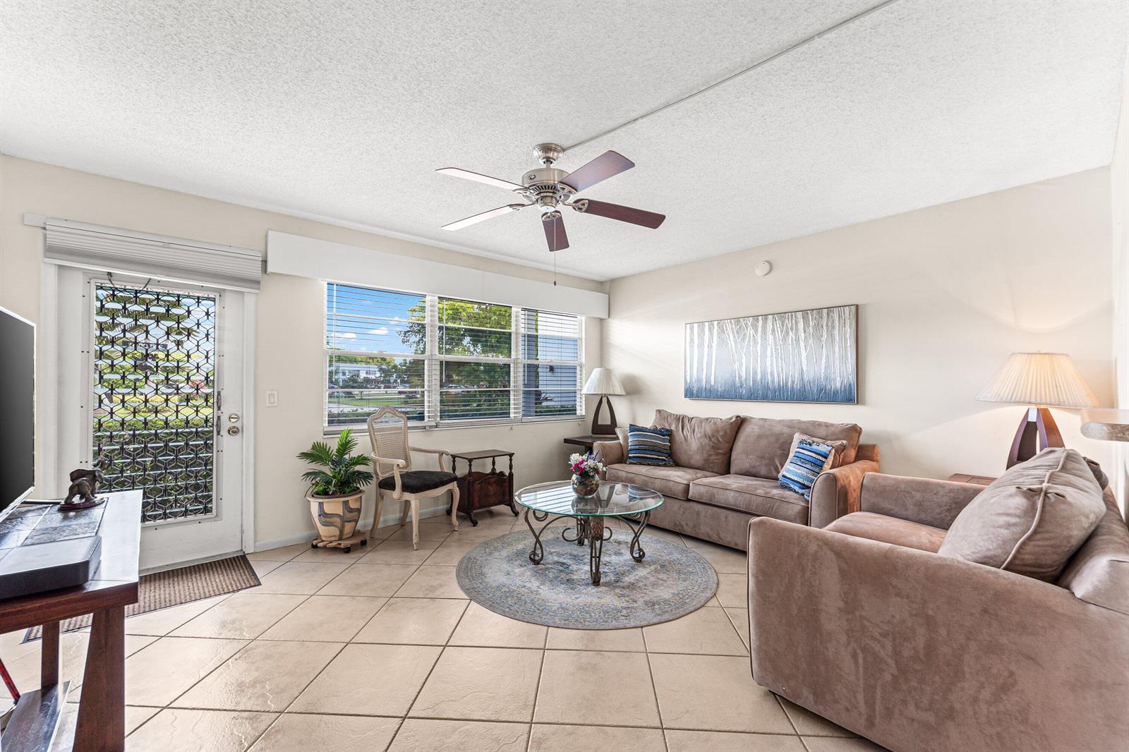 A living room features tile flooring, a ceiling fan, a sofa, and a glass-topped coffee table — 1017 Harwood C, Deerfield Beach FL 33442, DEERFIELD BEACH, FL