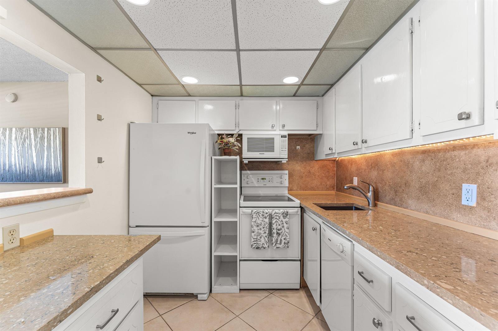 A kitchen features white cabinets, granite countertops, a white refrigerator, and a drop ceiling — 1017 Harwood C, Deerfield Beach FL 33442, DEERFIELD BEACH, FL