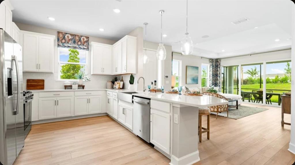 A modern kitchen with white cabinets, stainless steel appliances, and an island overlooks a living area — 7519 MOONBEAM AVENUE, SARASOTA, FL