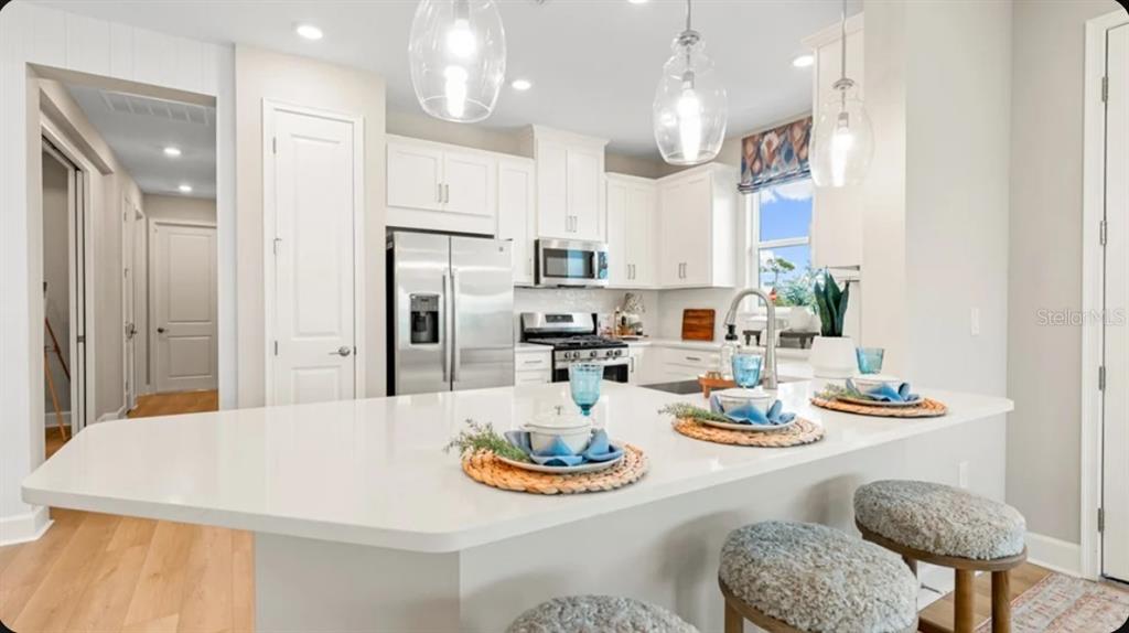 A modern kitchen features white cabinetry, stainless steel appliances, and a large quartz-topped island — 7519 MOONBEAM AVENUE, SARASOTA, FL