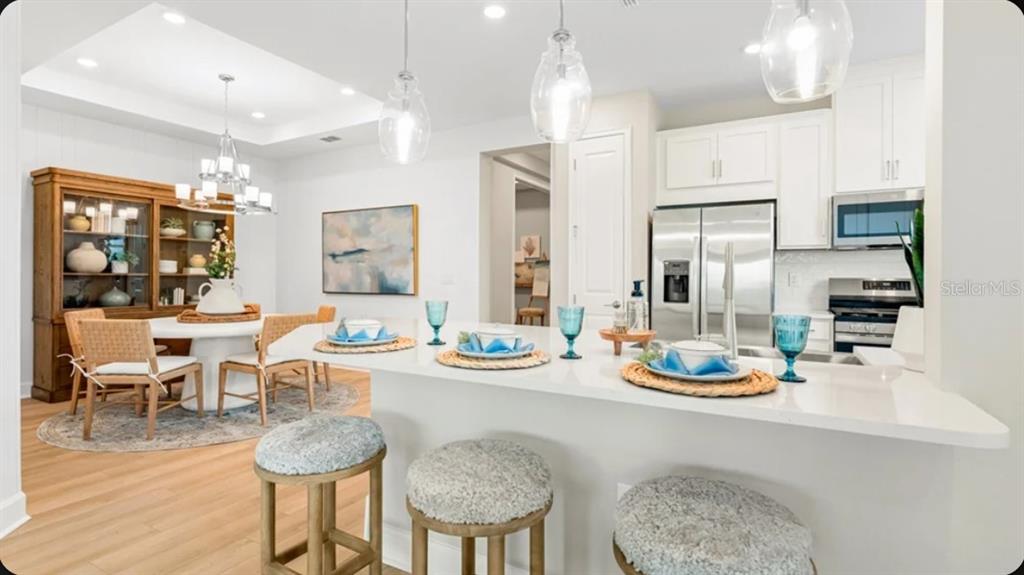 A kitchen with white cabinets and a breakfast bar overlooks a dining area with furniture — 7519 MOONBEAM AVENUE, SARASOTA, FL
