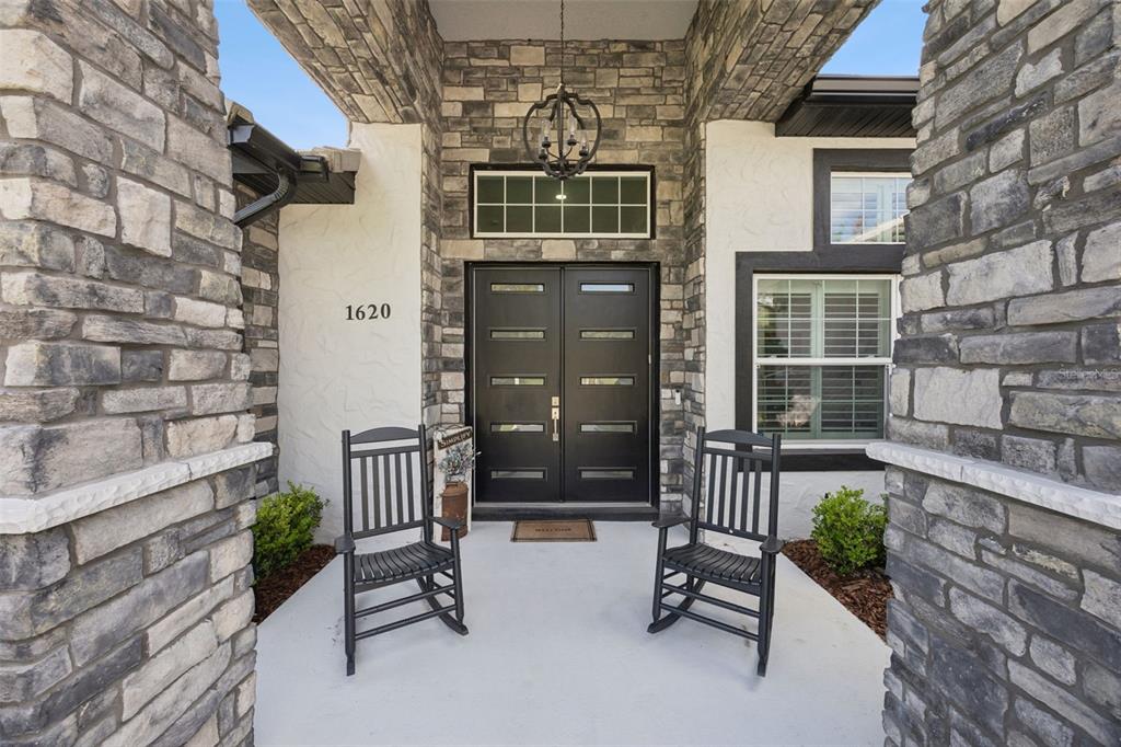 A front porch features two black rocking chairs flanking a double door entrance with stone — 1620 BOWMAN STREET, CLERMONT, FL