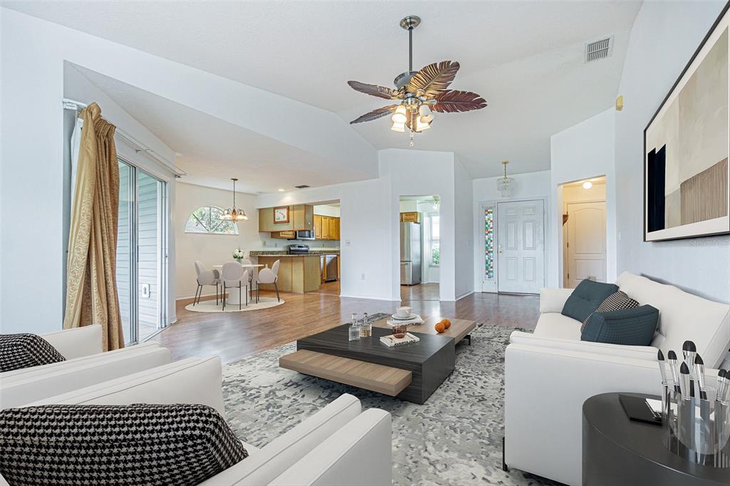 A bright living room with white furniture, a patterned rug, and an open-concept kitchen area — 11204 COREY PAVIN LANE, SAN ANTONIO, FL