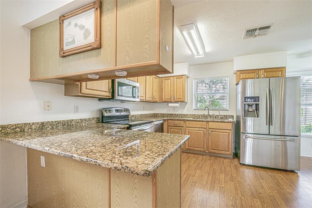 A kitchen features oak cabinets, granite countertops, stainless steel appliances, and wood-look flooring — 11204 COREY PAVIN LANE, SAN ANTONIO, FL