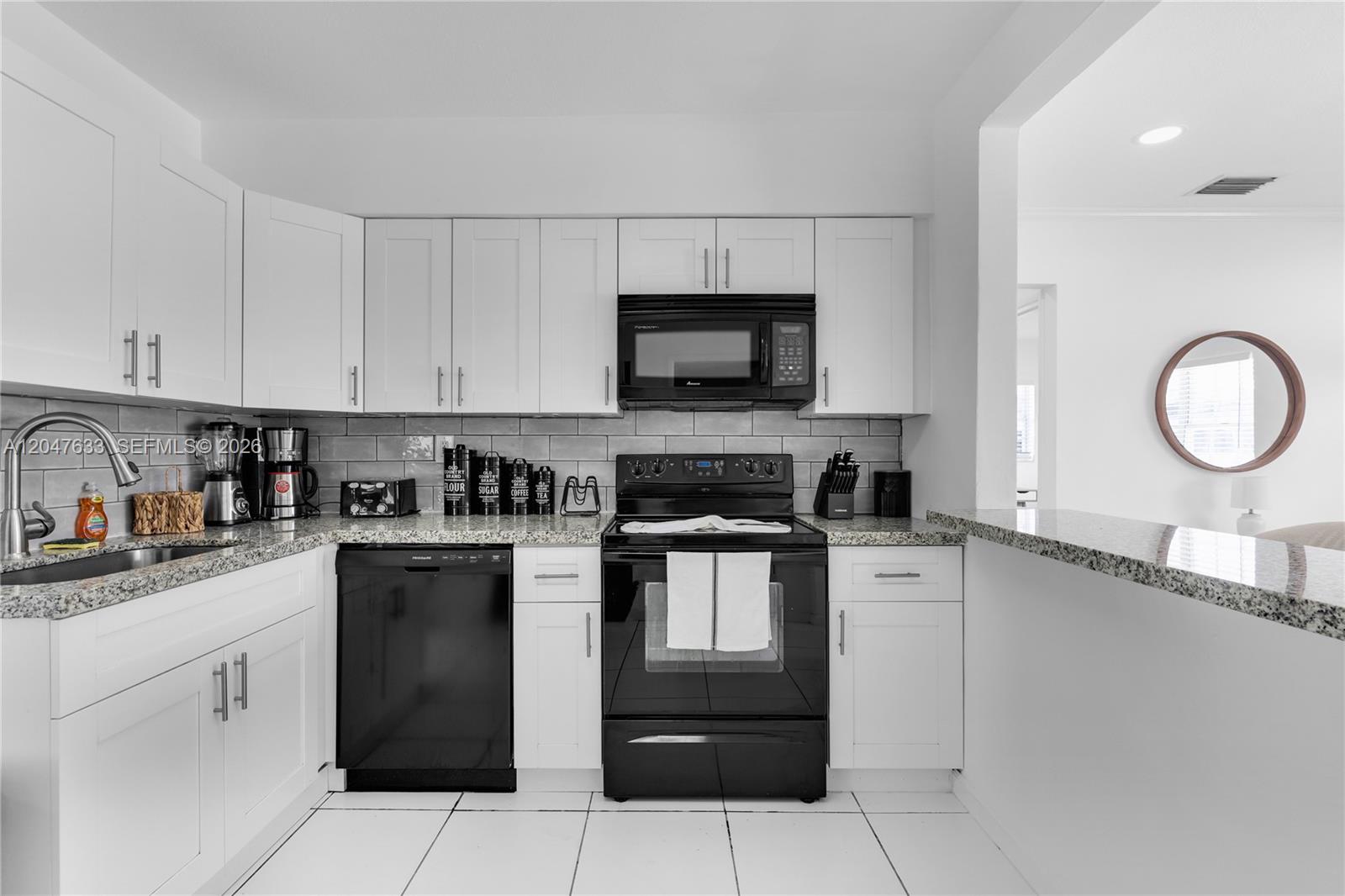 A kitchen features white cabinets, black appliances, granite countertops, and a gray subway tile backsplash — 6445 SW 22nd Ct, Miramar FL 33023, MIRAMAR, FL