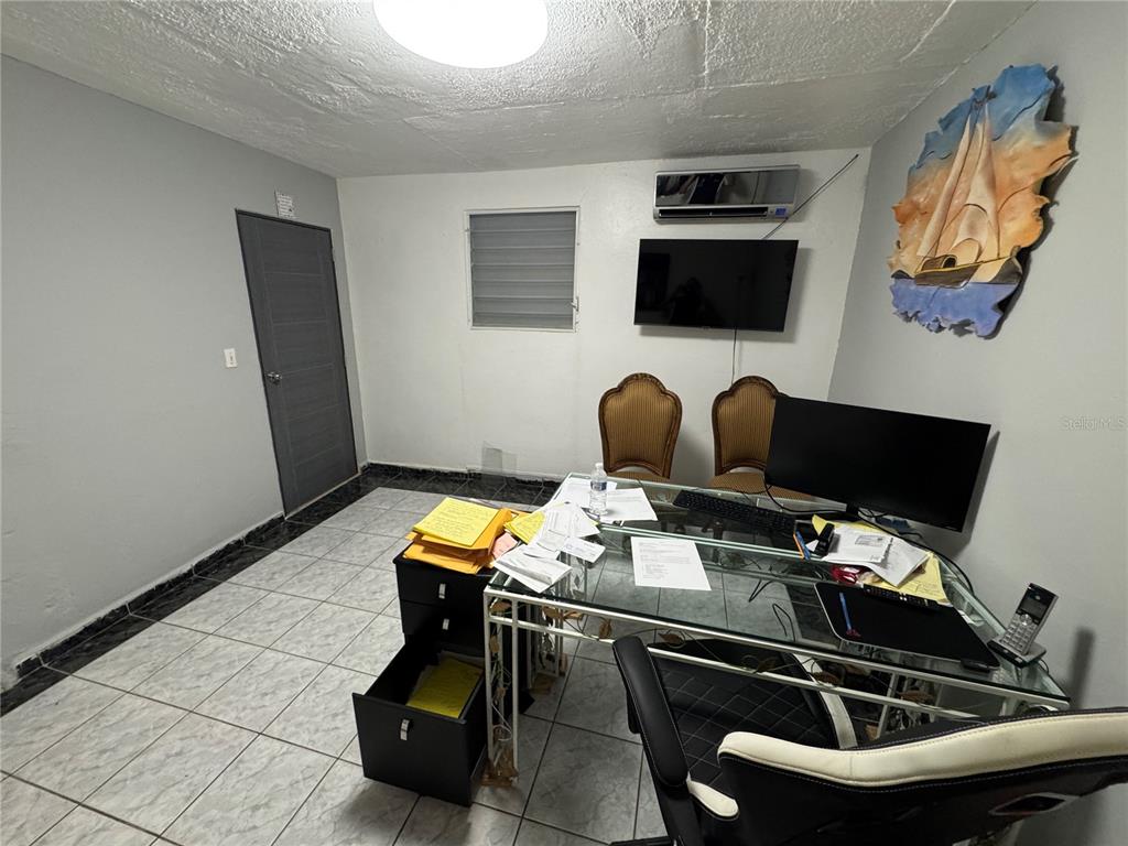 A home office features a glass desk, two chairs, a wall-mounted television, and tiled flooring — #339 COLL Y TOSTE, SAN JUAN, PR