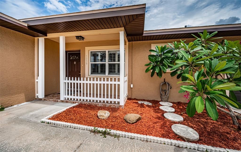 The exterior of a house features a tan stucco facade, a small porch, and landscaping — 1039 MADISON STREET, LARGO, FL
