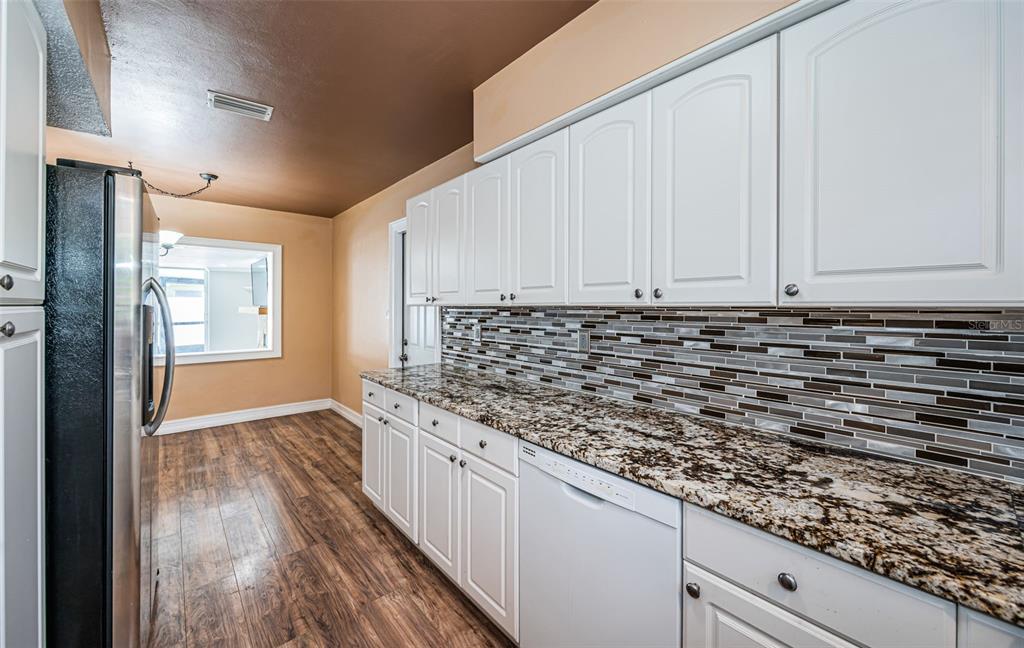 A kitchen features white cabinets, granite countertops, a mosaic tile backsplash, and wood-look flooring — 1039 MADISON STREET, LARGO, FL