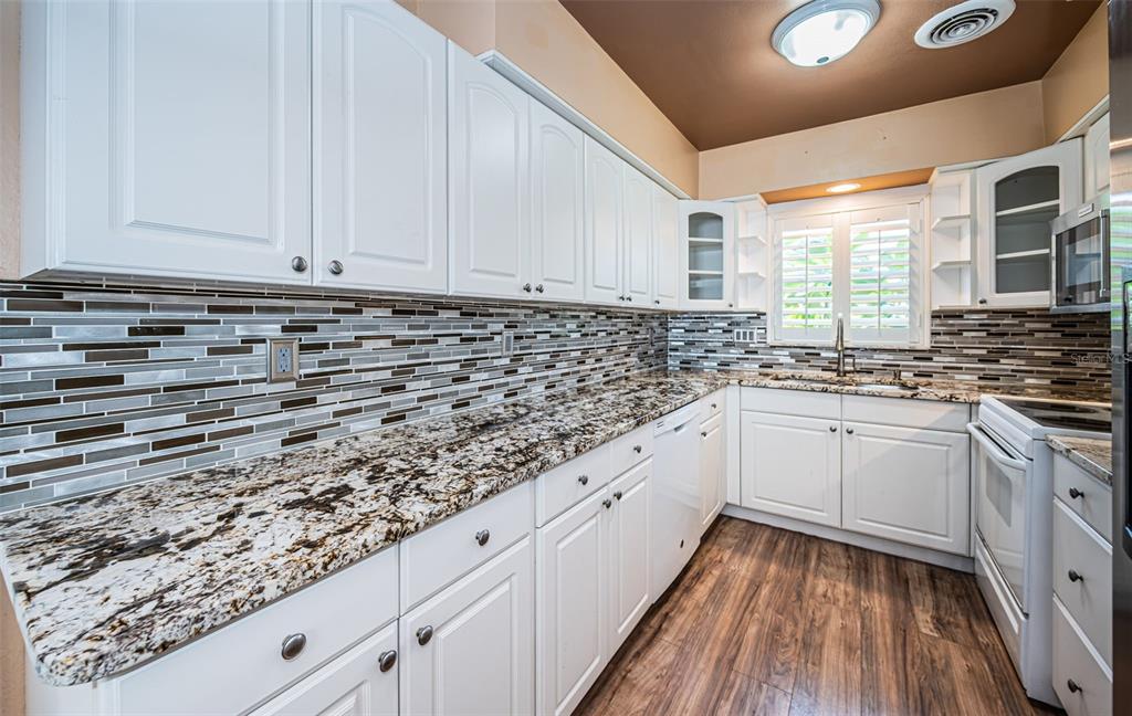 A kitchen with white cabinets, granite countertops, a mosaic tile backsplash, and wood-look flooring — 1039 MADISON STREET, LARGO, FL