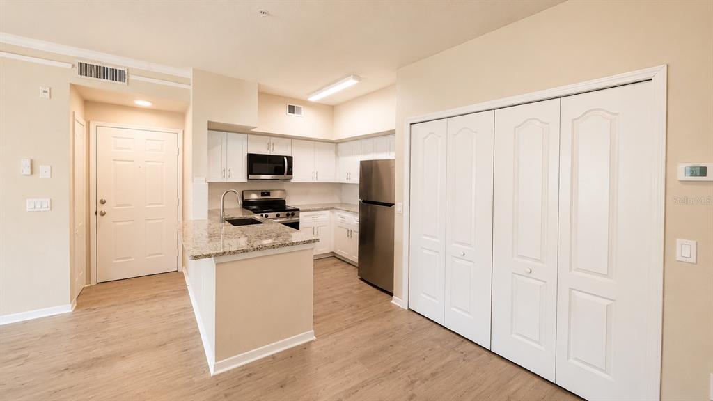 A kitchen features white cabinets, granite countertops, stainless steel appliances, and light wood-look flooring — 4142 CENTRAL SARASOTA PARKWAY UNIT 1423, SARASOTA, FL