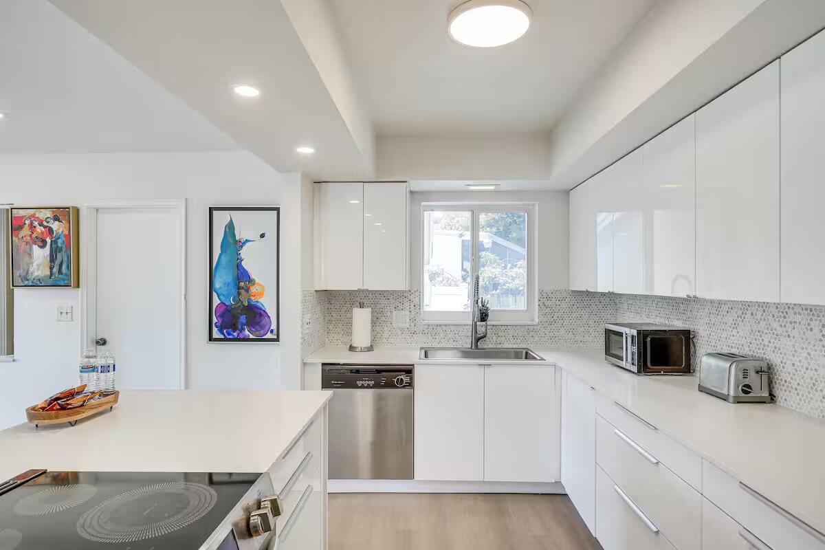 A modern kitchen features white glossy cabinets, stainless steel appliances, and a white island countertop — 124 SW 2nd Avenue, Hallandale Beach FL 33009, HALLANDALE BEACH, FL