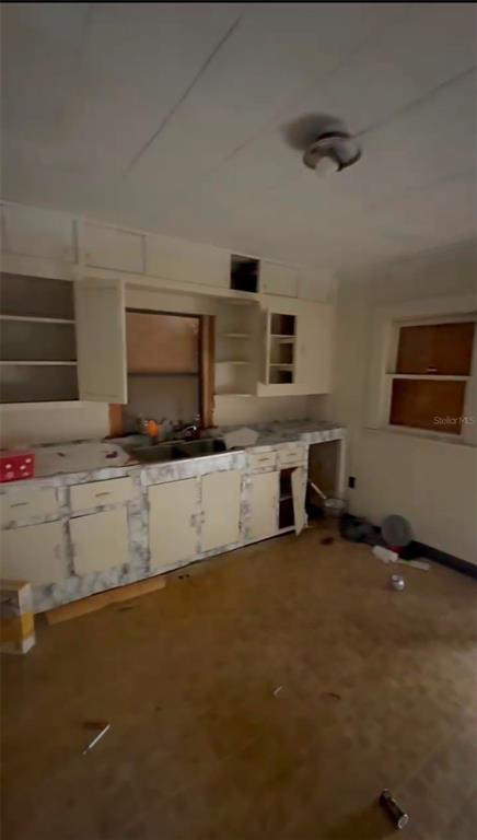 A dated kitchen features white cabinets, a double sink, and worn flooring in need of renovation — 2516 E MAGNOLIA STREET, LAKELAND, FL