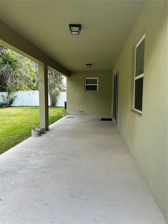 A covered concrete patio overlooks a grassy backyard enclosed by a white fence — 2581 MARSHFIELD PRESERVE WAY, KISSIMMEE, FL
