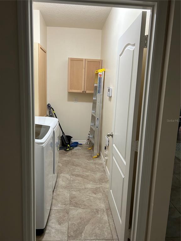 A laundry room features tile flooring, a white washer, wall-mounted cabinets, and a folding ladder — 2581 MARSHFIELD PRESERVE WAY, KISSIMMEE, FL
