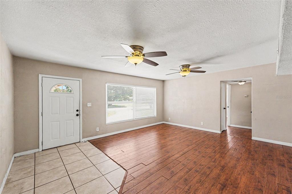 A living room features wood-look flooring, a tiled entryway, two ceiling fans, and white walls — 11428 75TH AVENUE, SEMINOLE, FL