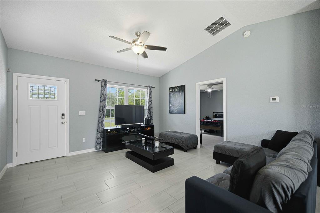 A living room features light gray walls, tile flooring, a vaulted ceiling, and black furniture — 17725 SW 31ST AVENUE, OCALA, FL